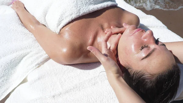 Üst manzarayı kapatın. Yaz boyunca kumsaldaki esmer kıza yüz masajı yapan masaj terapisti. Stresten rahatlama, baş ağrısı, sağlık yaşam tarzı ve vücut bakımı, rehabilitasyon konsepti