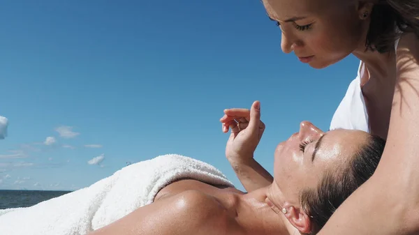 Близько. Жіночий масажист робить масаж шиї брюнетці на пляжі влітку, масаж процедури. Молода жінка насолоджується масажем на вулиці. Здоровий спосіб життя та концепція догляду за тілом — стокове фото