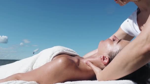 De aproape. Femeie masaj terapeut face masaj gât pentru fata bruneta pe plajă în timpul verii, procedura de masaj. O tânără se bucură de masaj afară. Stilul de viață sănătos și conceptul de îngrijire a corpului — Videoclip de stoc
