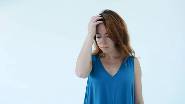 Mavi elbiseli ve kızıl saçlı ciddi bir kızın portresi düşünceli bir şekilde alnına ve saçlarına dokunuyor. Stüdyonun beyaz arka planında tek başına dikilip duruyor. Güzellik konsepti