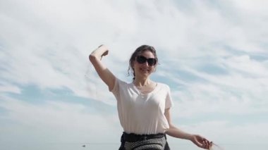 Beyaz tenli tatlı bayan sahilde mutlu ve gülümsüyor yaz mevsiminde bir avuç kuru kumu yakalıyor ve düşmesine izin veriyor. İyi eğlenceler.