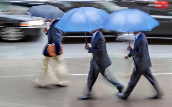 Mensen uit het bedrijfsleven lopen in de straat op een regenachtige dag beweging vervagen — Stockfoto