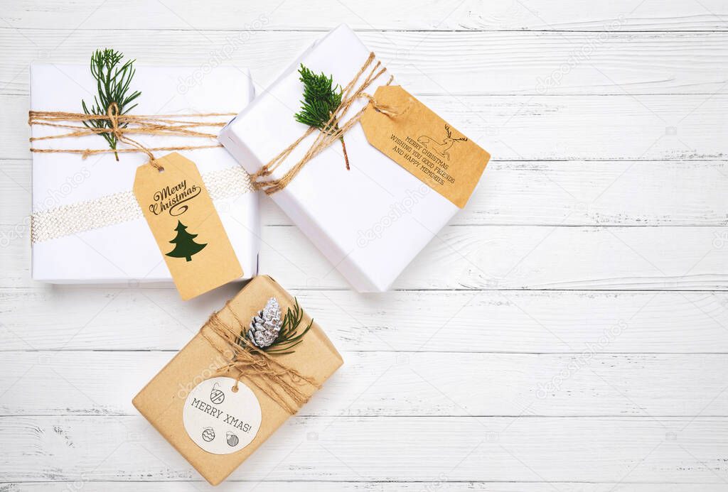 Christmas gift box with greeting tag - christmas present and pine leaves decoration on white wood table. Merry Christmas and New Year holiday background. top view.