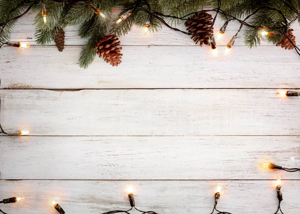 クリスマスの背景 クリスマスライト電球と松の葉の装飾白い木の板 フレームの境界線のデザイン メリークリスマスと新年の休日の背景 トップビュー — ストック写真