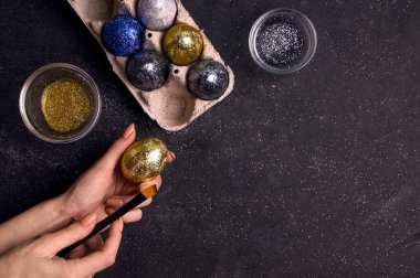 Paskalya için. Kız siyah arka planda parıltılı yumurta boyuyor. Uzayı kopyala Yukarıdan görüntüle