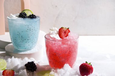 Gri bir arka planda buzlu ve dutlu soğuk kokteylli iki bardak..