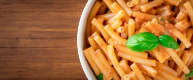 Sağlıklı organik İtalyan makarnası ev yapımı makarna makarna makarna makarna fesleğen domates, sarımsak biber sosu vejetaryen vejetaryen tarifi ile ahşap masadaki beyaz kasede pişiriliyor.