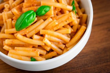 Sağlıklı organik İtalyan makarnası ev yapımı makarna makarna makarna makarna fesleğen domates, sarımsak biber sosu vejetaryen vejetaryen tarifi ile ahşap masadaki beyaz kasede pişiriliyor.