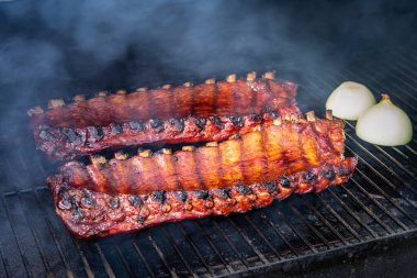 Arka planda görünür duman ve soğan yarımları olan ızgara tabaklarında oturan 2 kaburga.