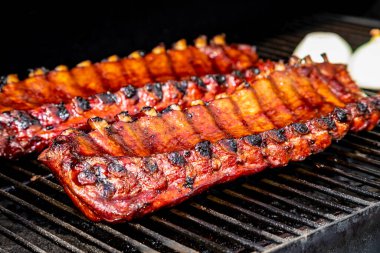 Barbekü soslu iki raf bbq kaburgası arka planda soğan yarısıyla ızgara tabağında oturuyor.