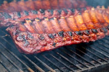 Barbekü soslu iki sıra bbq kaburgası yakın. Izgara tabaklarının üzerinde görünür bir duman var.