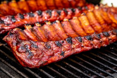 Barbekü soslu, ızgara tabaklarının üzerinde oturan ve arka planda beyaz soğan yarımları olan 2 adet bbq kaburgasını kapat.