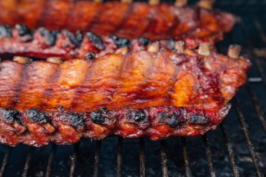 Barbekü soslu, dışarıda ızgara tabaklarında pişirilen iki raf bbq kaburgasının yan görüntüsünü kapatın.