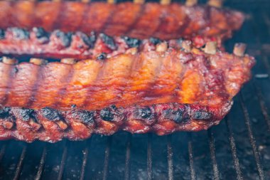 Barbekü soslu, dumanlı ızgarada pişirilmiş, sigara içen kişinin görünür dumanıyla çevrili 2 adet bbq kaburgasının yan görüntüsünü kapatın.