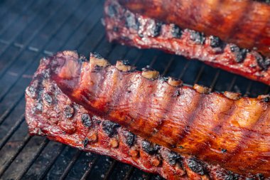 Yandan 2 sıra bbq pirzolası ve barbekü sosu ızgara tabağında pişiyor. İçicinin görünür dumanıyla çevrili.