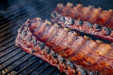 Yandan 2 sıra bbq pirzolası. Izgarada barbekü sosu pişiyor. İçicinin görünür dumanıyla çevrili.