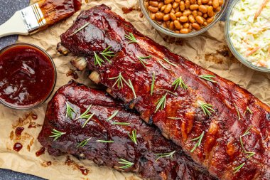 Barbekü sosu fırçası, lahana salatası, fırında fasulye ve taze kekik otlarıyla süslenmiş iki dilim pirzola.