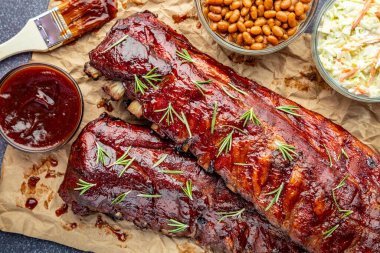 Barbekü sosu fırçası, lahana salatası, fırında fasulye ve taze kekik otlarıyla süslenmiş kahverengi kağıdın üzerinde oturan 2 parça kaburgayı kapatın.