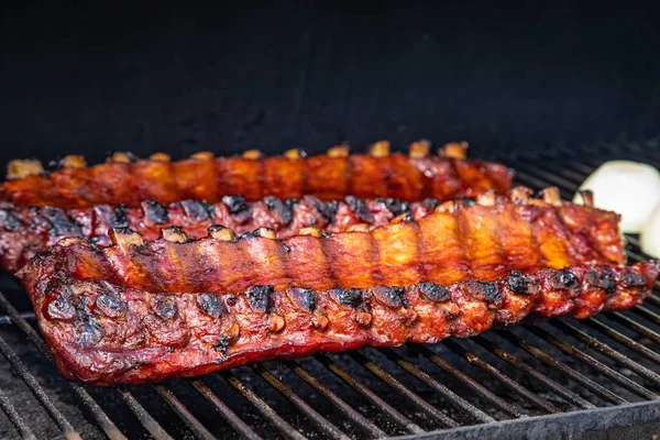 Barbekü soslu 2 dilim kaburga ızgara tabağında soğan yarımları ile oturuyor.