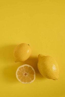 İki koca limon ve bir dilimlenmiş limon sarı bir yüzeye yerleştirilir. Dilim, içerideki sulu şeyi ortaya çıkarıyor. Canlı ve göz alıcı içerik sahnesi.