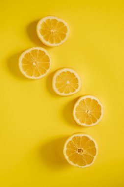 Limonlar dilimlenir ve parlak sarı arka planda bir çizgiye yerleştirilir. Limon yarımları sulu iç ve parlak renklerini gösteriyor. Ayarlar basit ve taze..