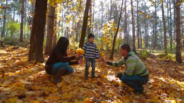 Jeune famille avec un petit garçon ramassant des feuilles jaunes dans le parc d'automne 