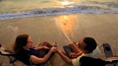 Romantik çift el ele tutuşuyor ve plajda açık sandalyede otururken konuşuyor