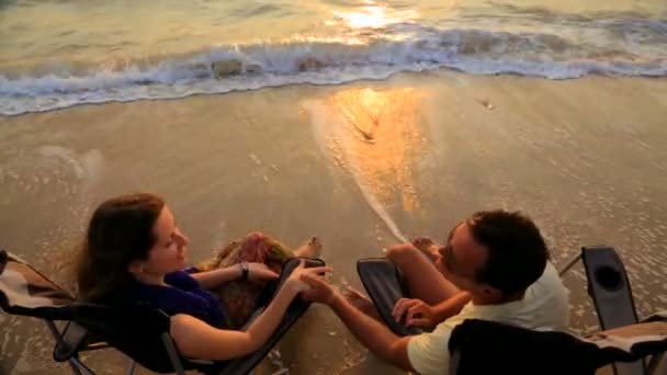 Romantisches Paar hält Händchen und spricht, während es am Strand auf Liegestühlen sitzt — Stockvideo