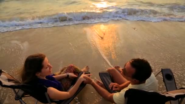 Romantisch paar houdt handen en praten terwijl zittend op buiten stoelen op het strand — Stockvideo