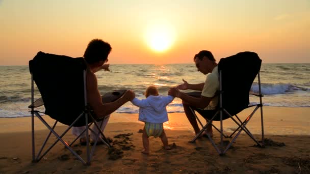 Dos hombres en sillas al aire libre y bebé en la playa al atardecer — Vídeos de Stock