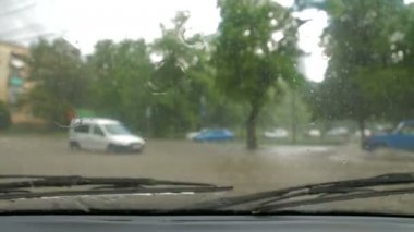 Arabanın ön camına yağmur damlalarının yakın çekimi. Ön cam silecekleri açık.