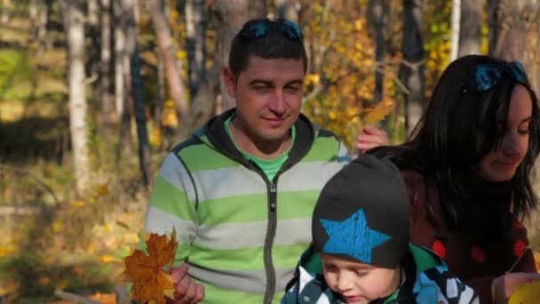 Portret van een jong gezin met een kind het oppakken van gele bladeren in Autumn Park — Stockvideo