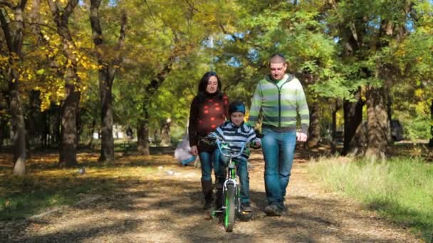 Ευτυχισμένος νέος οικογένεια με ένα παιδί με ποδήλατο περπάτημα στο φθινόπωρο πάρκο — Αρχείο Βίντεο