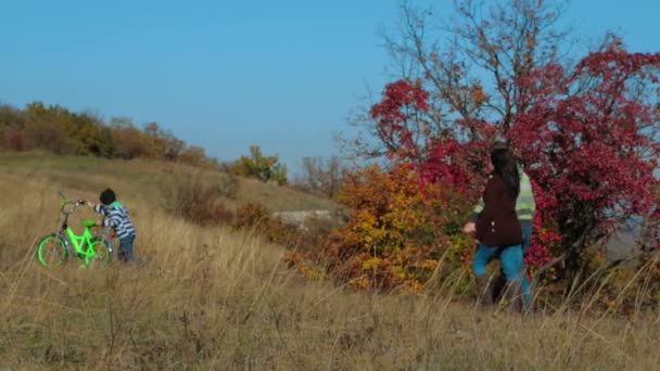 Gelukkig jong gezin met een kind op fiets wandelen in de herfst weide — Stockvideo