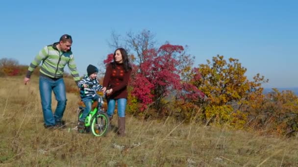 Familia joven feliz con un niño caminando en el prado de otoño — Vídeo de stock