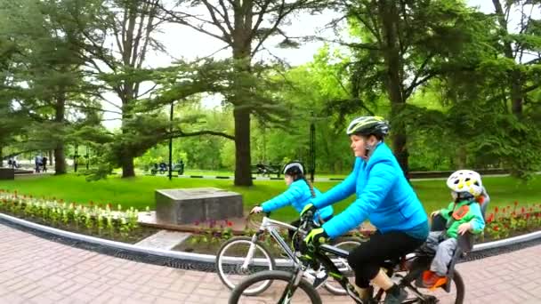 Молодая мать с двумя детьми на велосипедах в зеленом парке — стоковое видео