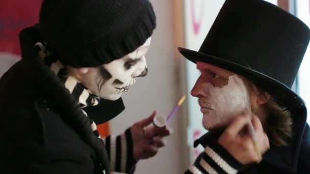 Mujer joven aplicando maquillaje en la cara de los hombres en Halloween — Vídeo de stock
