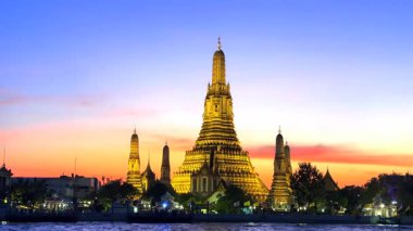 Wat Arun gün batımında altın ışıkta parlıyor, Tayland 'ın Bangkok şehrinde Chao Phraya nehrinin üzerinde dramatik bir akşam gökyüzü altında yansıyor..