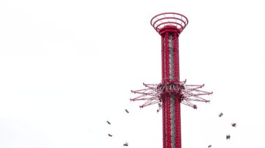 Yükselen kırmızı bir gökyüzü salıncak, yerden yükseğe doğru dönüyor, sürücüler parlak mavi bulutlarla dolu gökyüzüne karşı hareket halindeler..