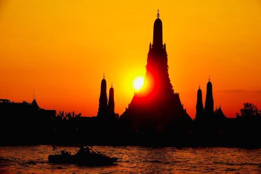 Bangkok 'taki Wat Arun Tapınağı' nın gölgesinin arkasındaki altın günbatımı Chao Phraya Nehri 'ne yansıdı. Dramatik gökyüzü, parlayan güneş ve ikonik Tayland mimarisi dingin ve zamansız bir seyahat sahnesi yaratır..