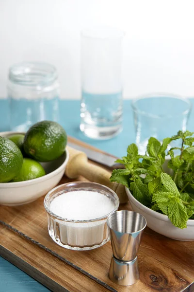 Mojito kokteyli malzemeleri ve tahta kesme tahtasındaki aletler. Mavi tablo ve beyaz arkaplan