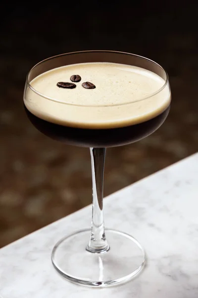 Espresso Martini, üç kahve çekirdeğiyle süslenmiş, mermer bir masada.