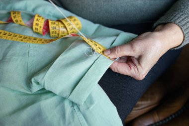 Yaşlı kadın dikiş dikiyor ve evde taksimetre kullanıyor.