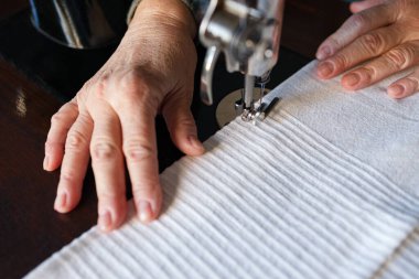 Yaşlı kadın elleri eski bir dikiş makinesi kullanıyor.