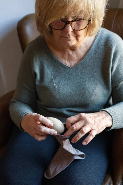 Old woman mending a sock at home