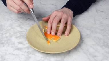 Bir adamın eli, bir portakalın derisini bıçakla kesiyor. Takma diş.