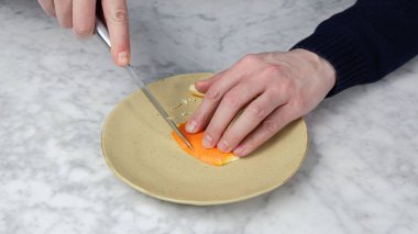 Bir adamın eli, bir portakalın derisini bıçakla kesiyor. Takma diş.