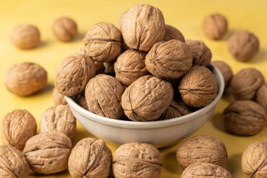 Sarı arka plandaki bir kasenin içindeki ceviz yığınına yakın plan.