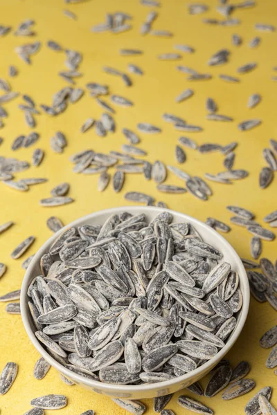 Pile of salted and roasted sunflower seeds in a bowl on a yellow background
