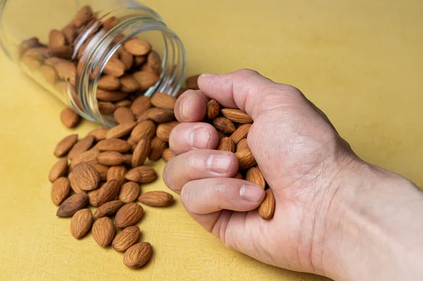 Hand grabbing a pile of peeled almonds from a yellow table